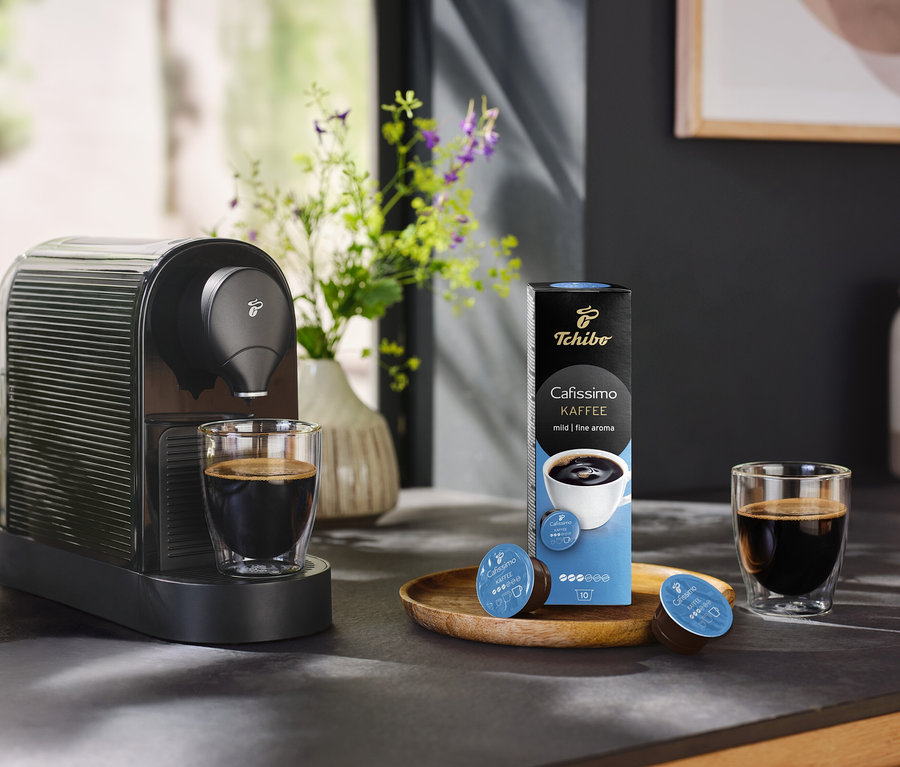 Ekspres do kawy stoi obok szklanki kawy i opakowania 10 kapsułek Coffee Mild.