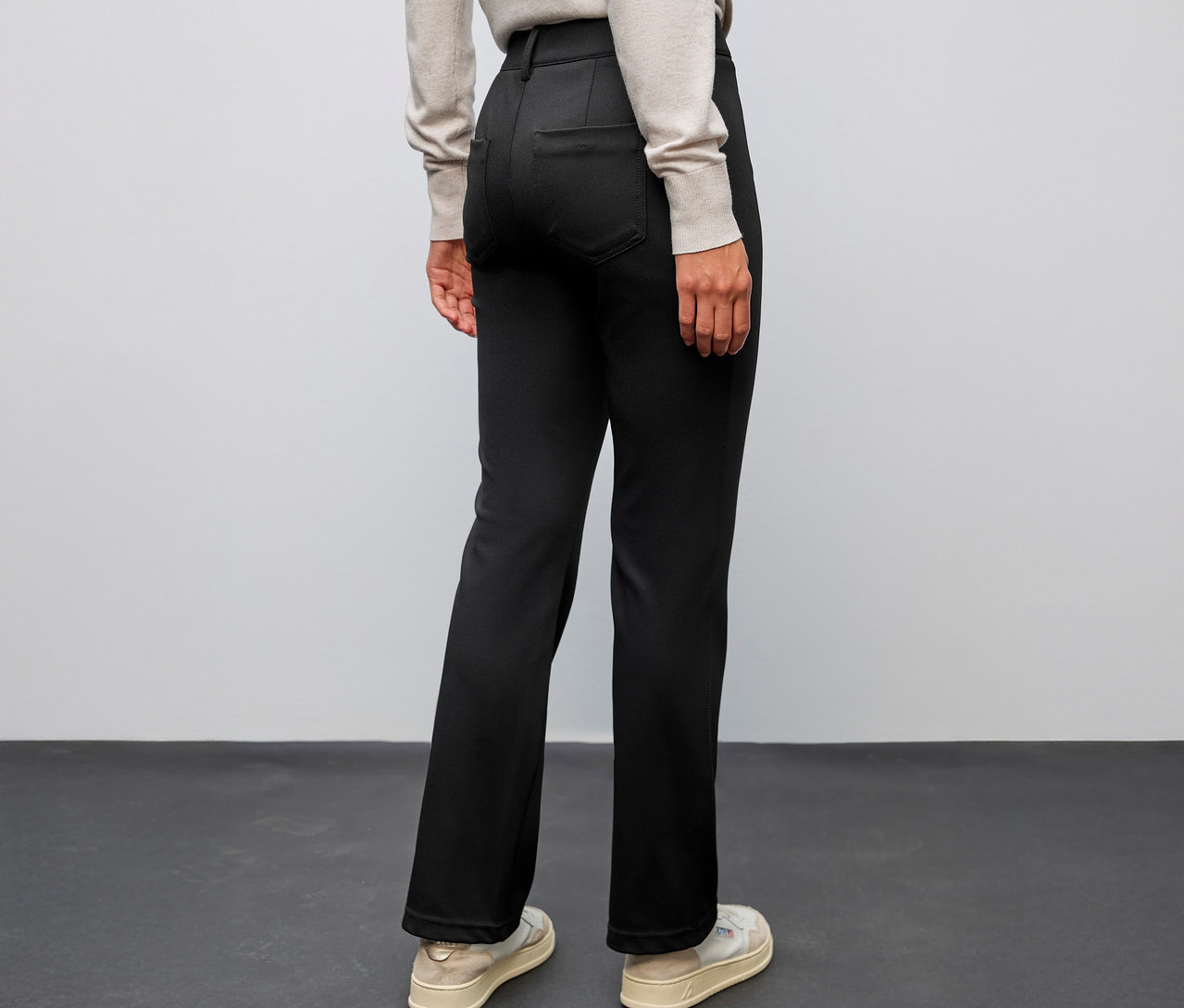 Osoba widziana od tyłu, ubrana w czarne spodnie dzwony Street One i jasne buty.