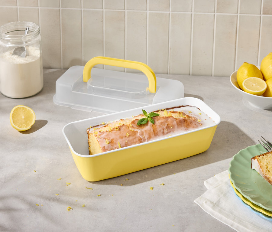 Ciasto cytrynowe w żółtej formie z cytrynami i lukrem, pokrojone na talerzu z widelcem.