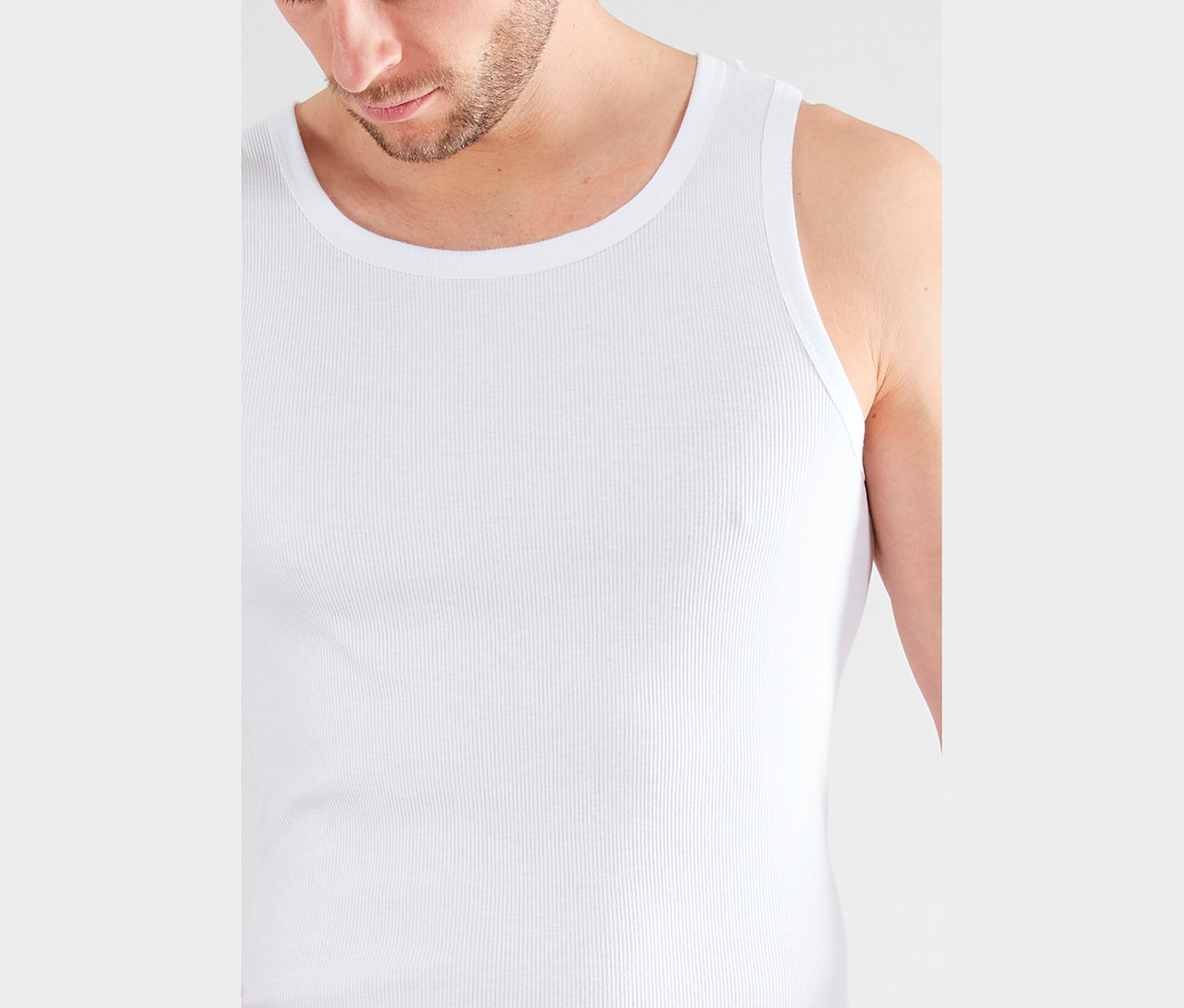 Zbliżenie mężczyzny z brodą w białym prążkowanym podkoszulku.