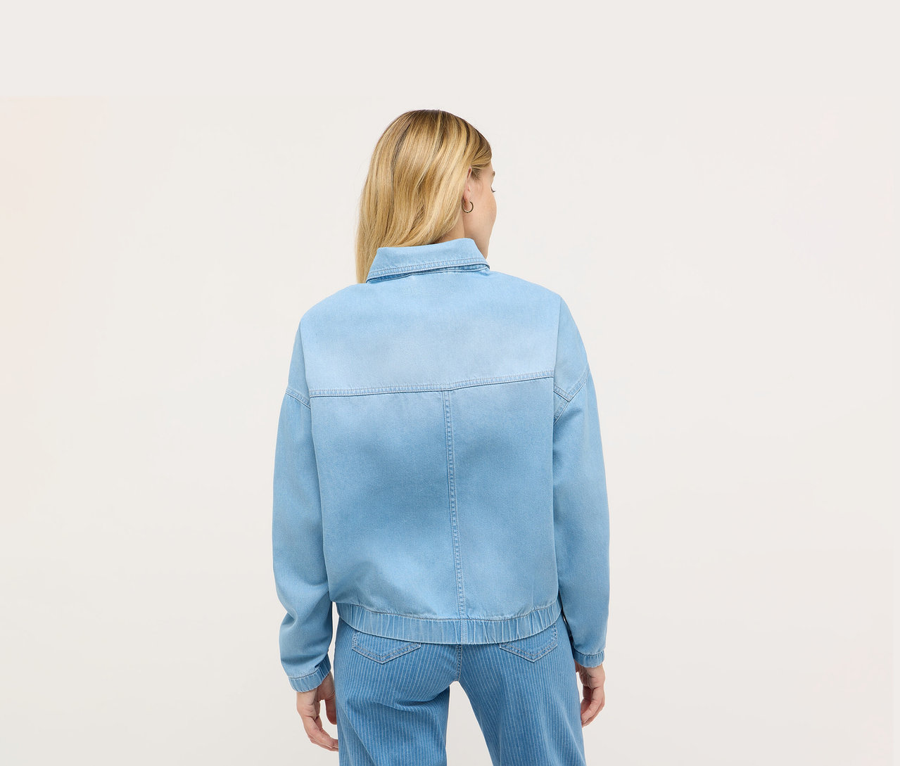 Widok z tyłu blondwłosej kobiety w niebieskiej kurtce dżinsowej Angels.