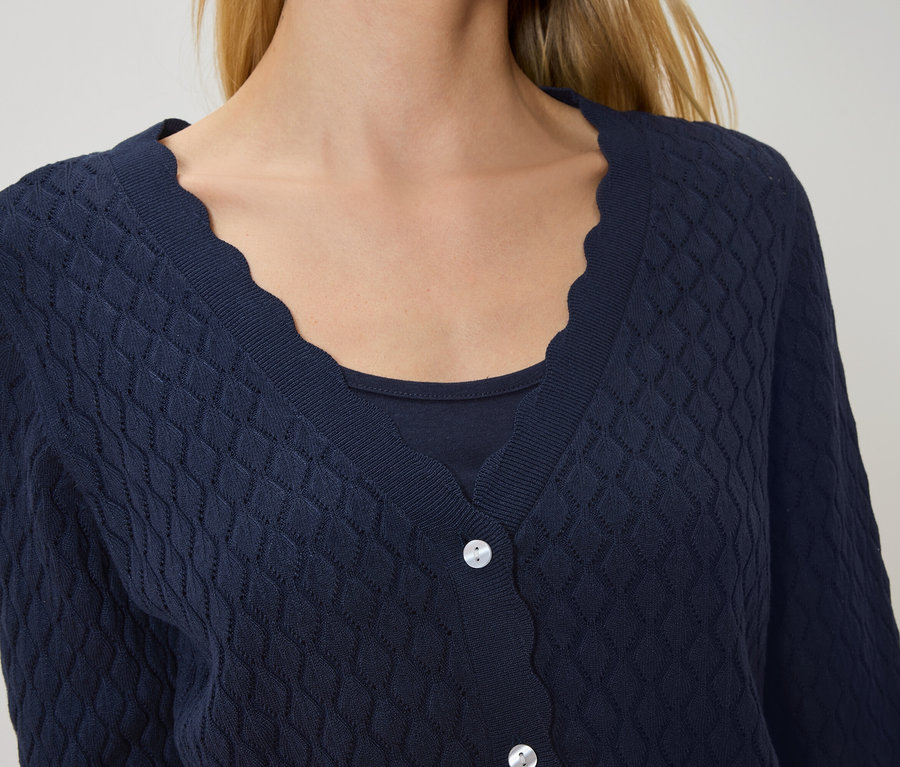 Kobieta ma na sobie granatowy kardigan z falistym brzegiem na granatowej bluzce.