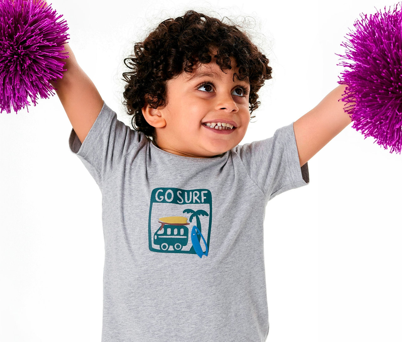 Uśmiechnięty chłopiec z kręconymi włosami w piżamie dziecięcej SCHIESSER trzyma fioletowe pompony.