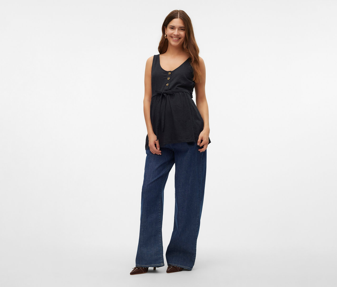 Uśmiechnięta kobieta ma na sobie top do karmienia piersią MAMALICIOUS „MLEVI LIA”, dżinsy i buty.