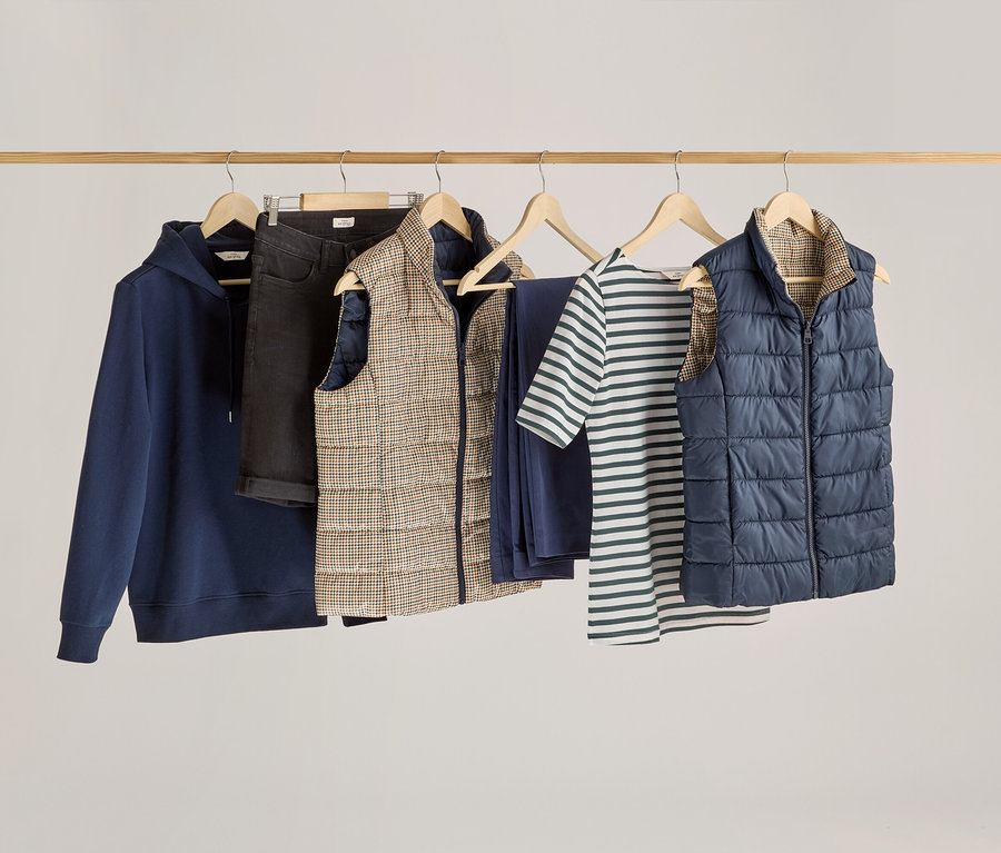 Ubrania wiszą na drewnianym drążku, w tym koszulka z półdługim rękawem w zielone paski.