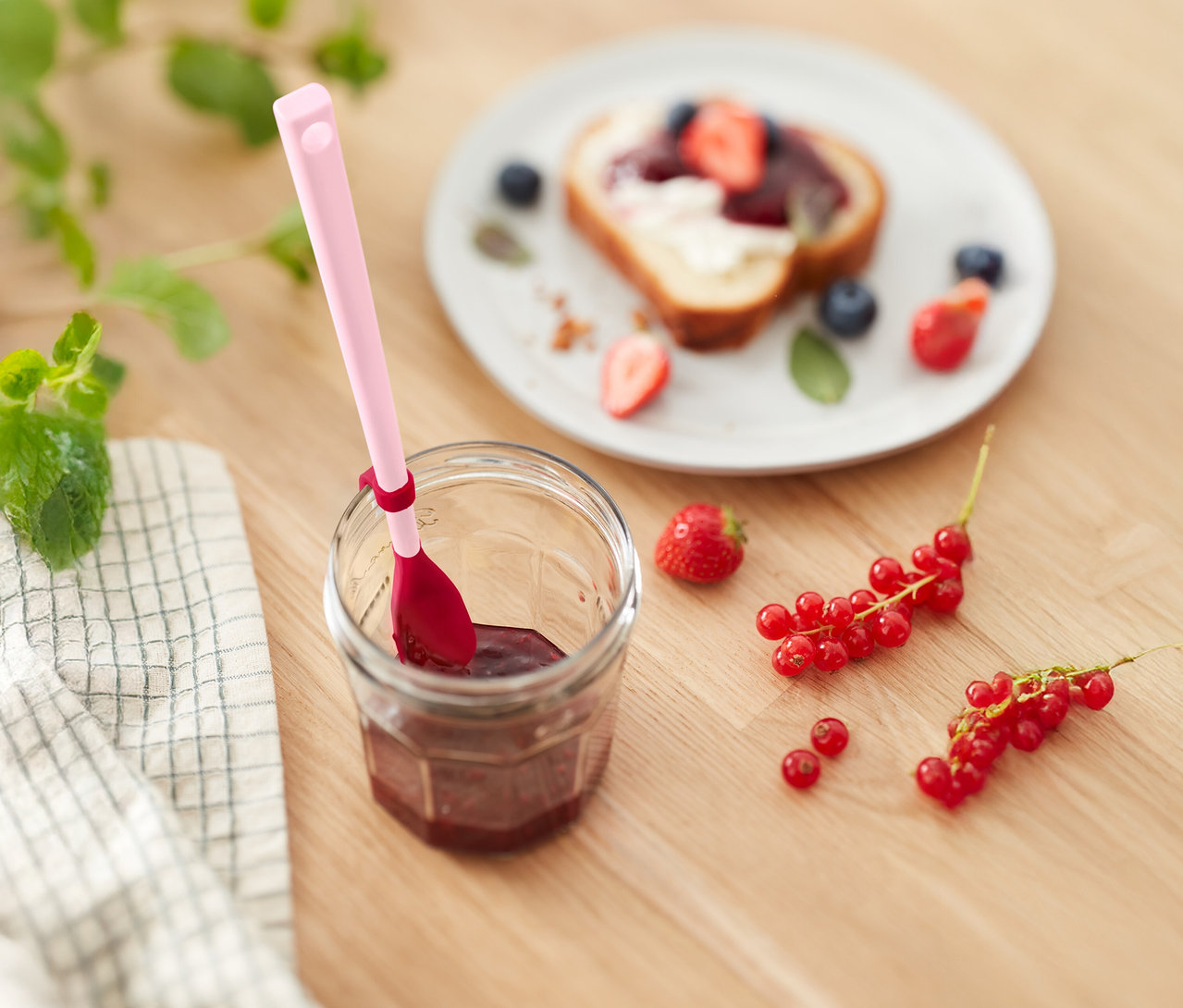 Słoik dżemu z różową łyżką, tost z truskawkami i jagodami oraz porzeczki na drewnianym stole.