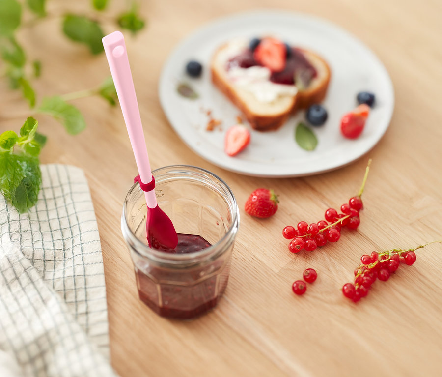 Słoik dżemu z różową łyżką, tost z truskawkami i jagodami oraz porzeczki na drewnianym stole.