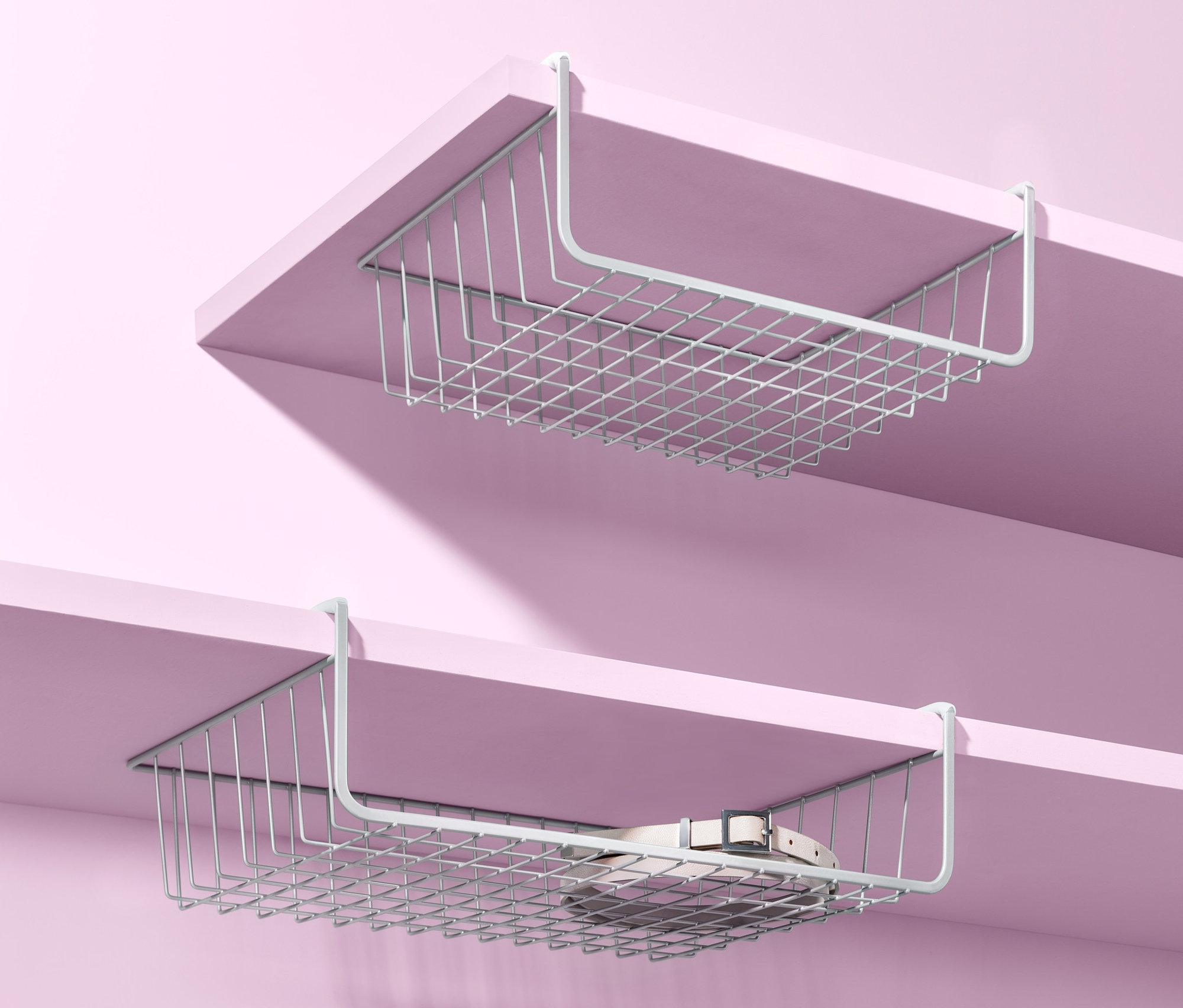 Dwa koszyki podwieszane do szafy wiszą pod półkami na różowym tle.