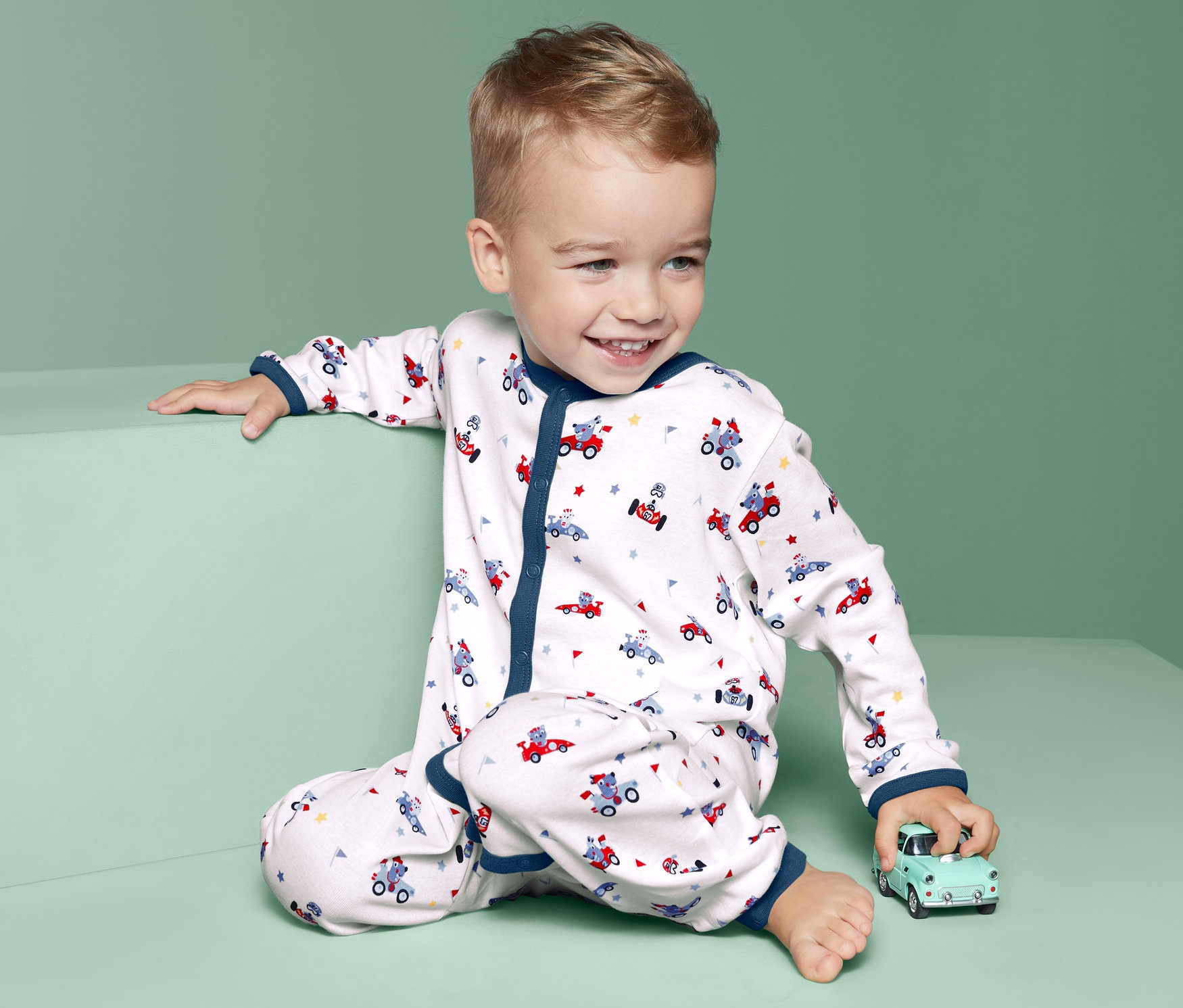 Uśmiechnięty chłopiec siedzi z zabawką i ma na sobie śpioszki pajacyki bawełniane z długimi rękawami, 2 sztuki.