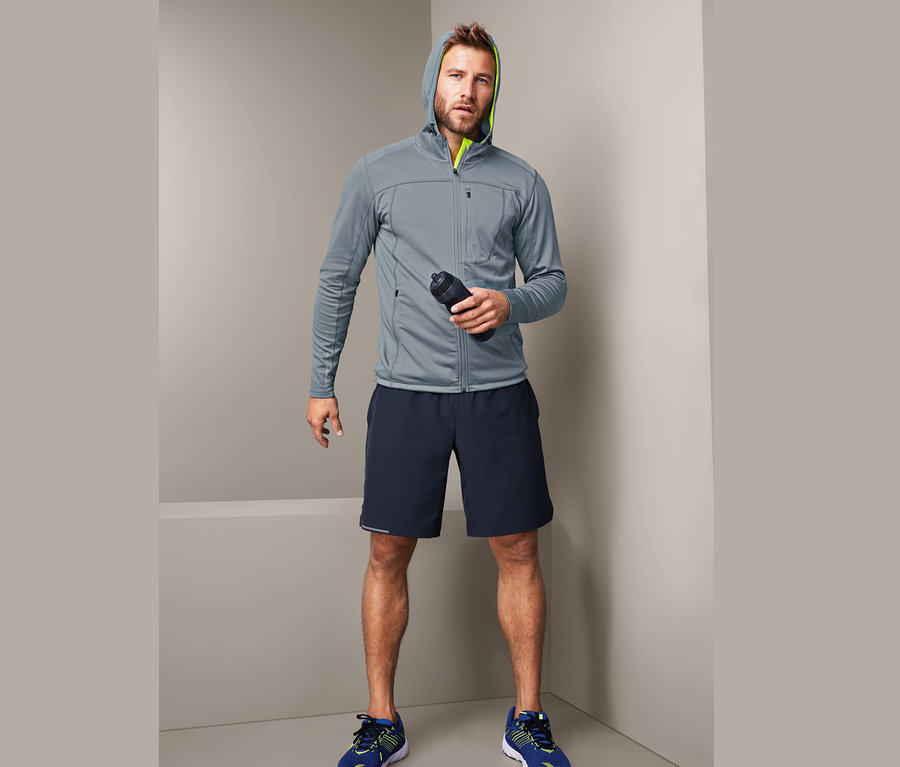 Mężczyzna w szarej bluzie sportowej trzyma butelkę z wodą.