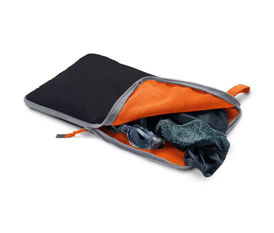 Otwarta czarna podkładka 2 w 1: podkładka pod nogi i worek na mokre rzeczy z pomarańczowym wnętrzem, w którym znajdują się okulary pływackie i strój kąpielowy.