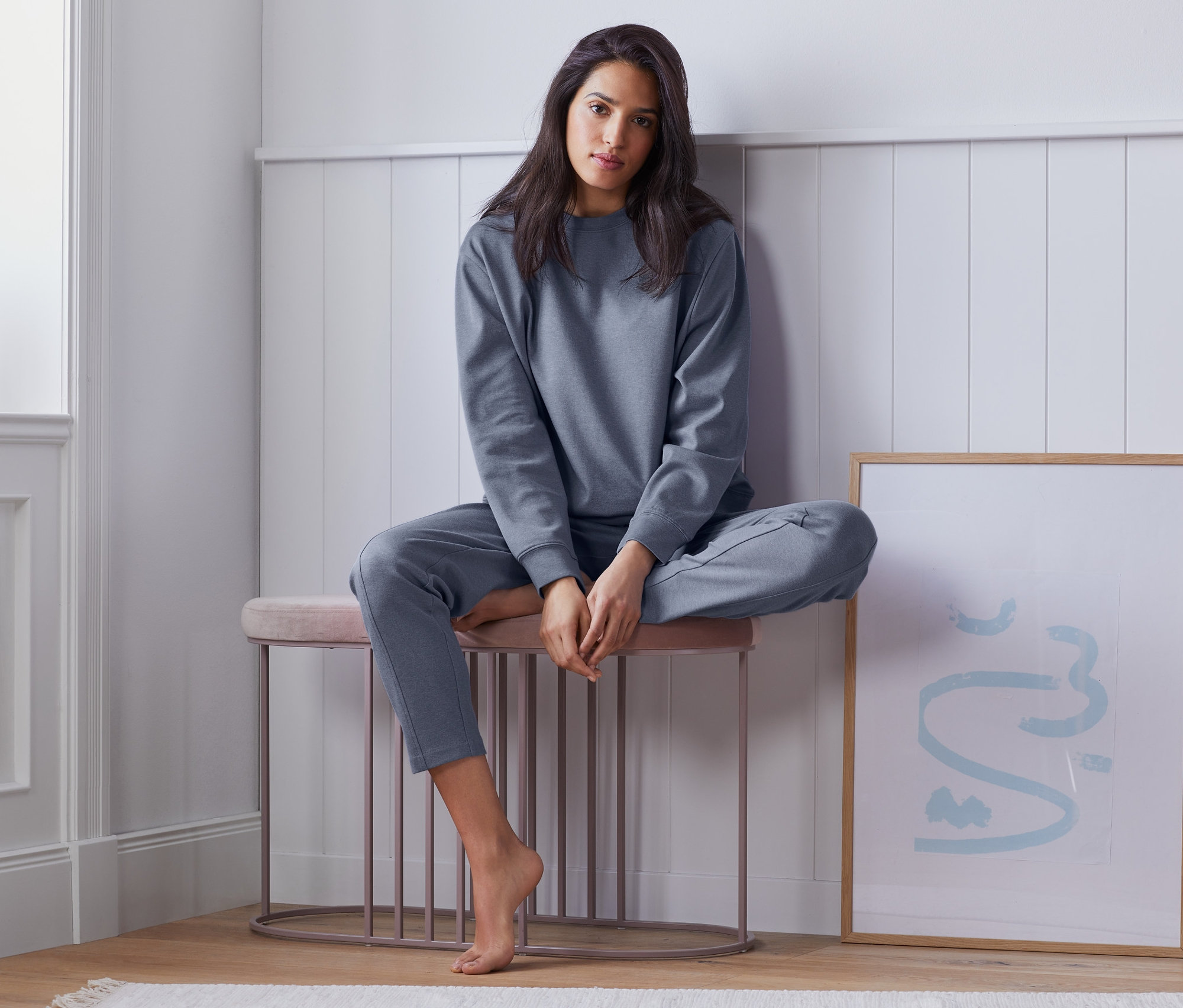 Kobieta siedzi na stołku w bluzie rekreacyjnej i spodniach.