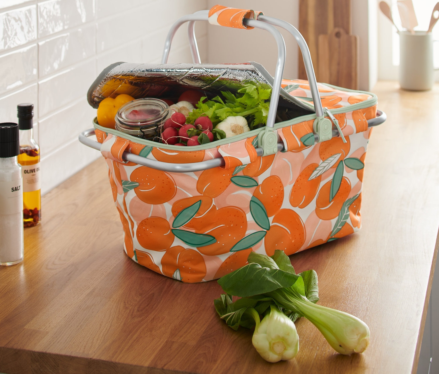 Koszyk termiczny w brzoskwiniowy wzór, pełen jedzenia, stoi na blacie kuchennym.
