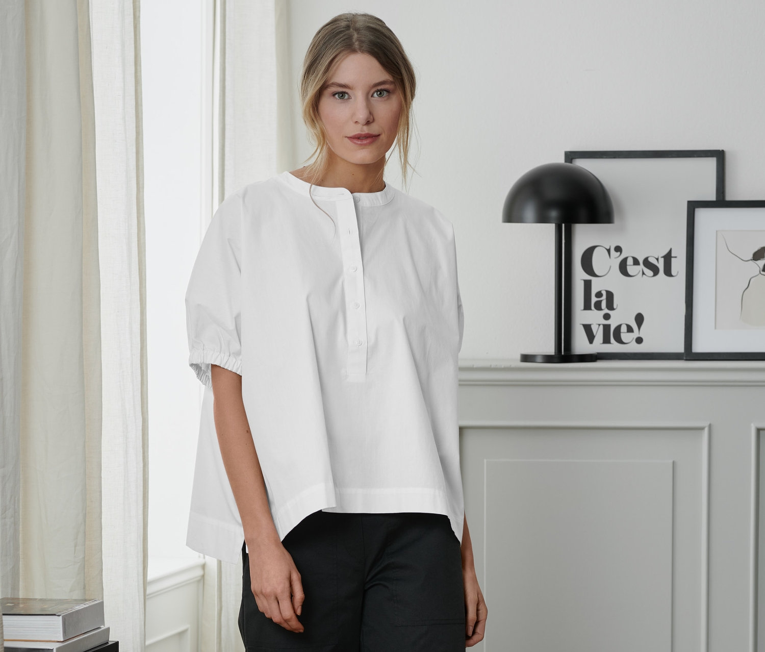 Kobieta stoi w białej bluzce z popeliny i czarnych spodniach.