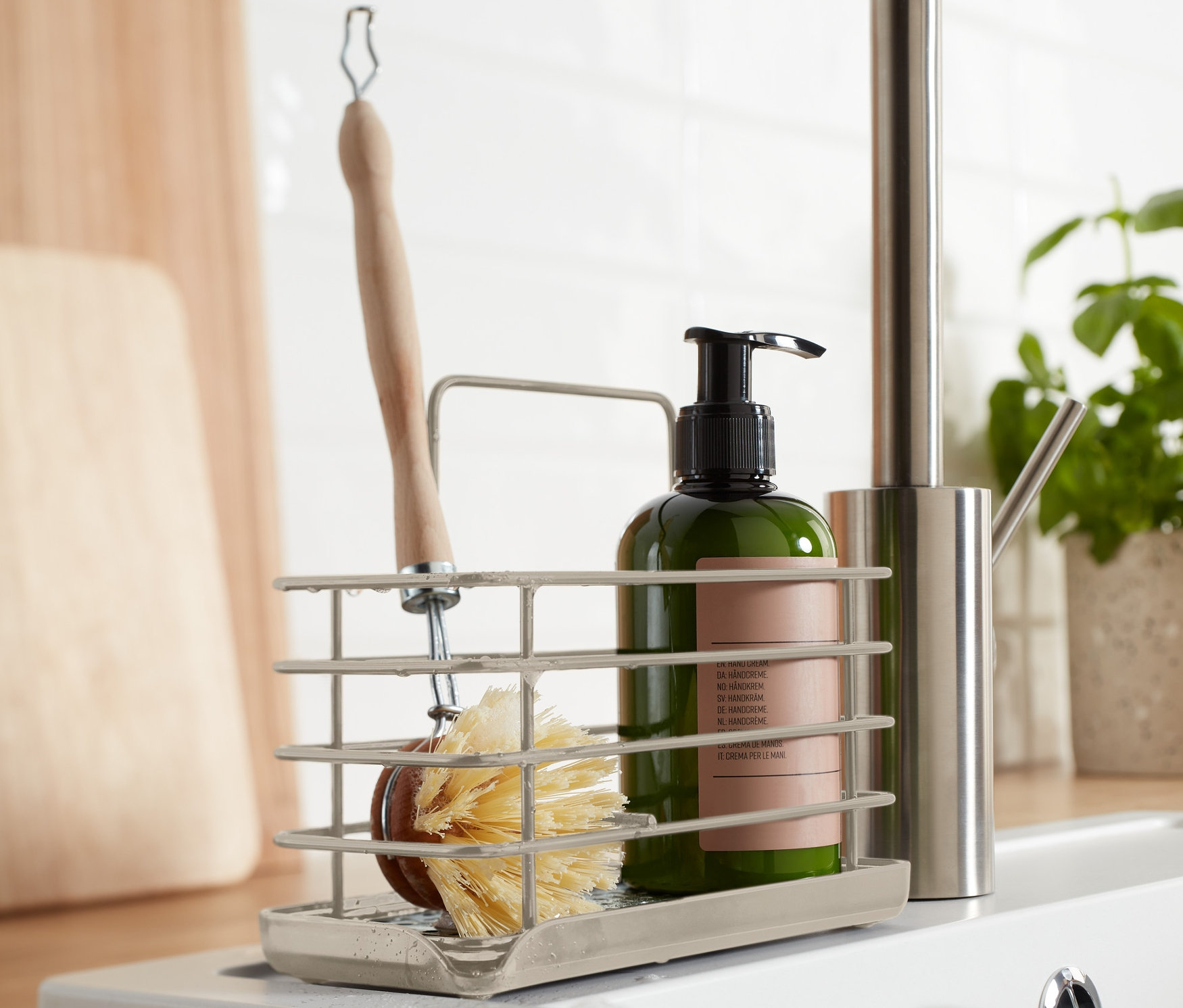 Szczegół metalowego stojaka na przybory kuchenne ze szczotką i butelką obok zlewu.