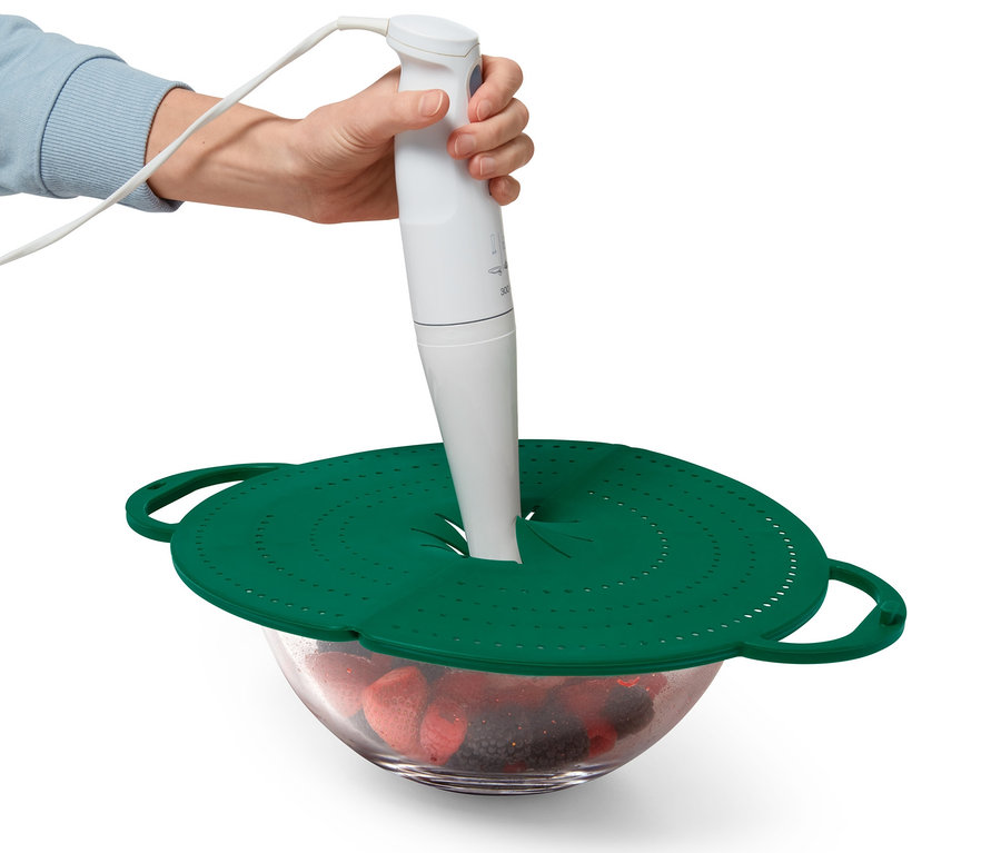 Ręka trzyma blender zanurzeniowy nad miską z owocami, miska jest przykryta zieloną osłoną na patelnię 4 w 1.