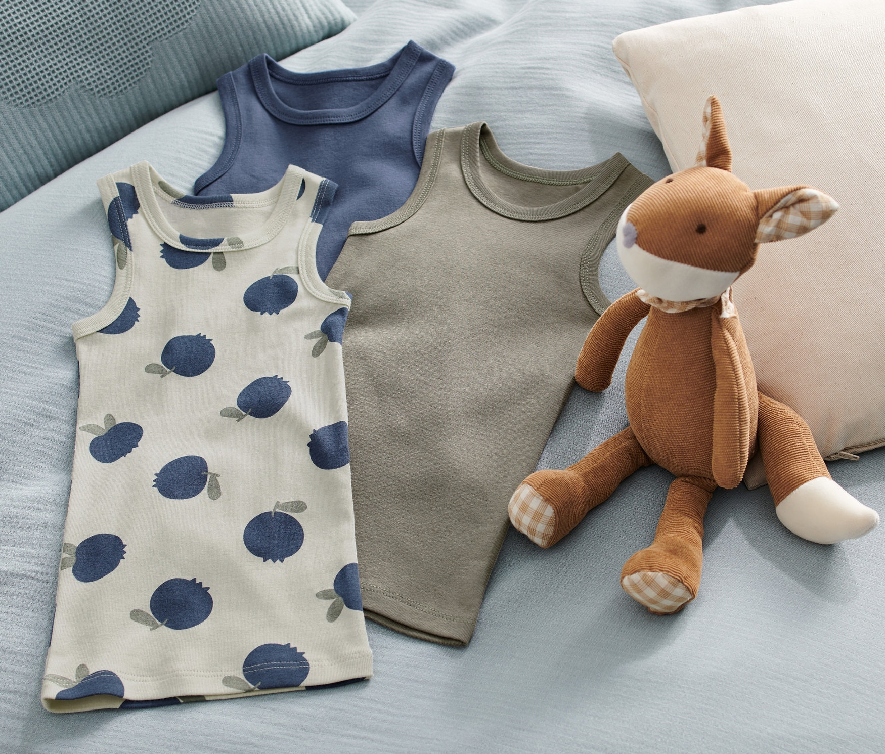 Na łóżku leżą trzy podkoszulki dziecięce w jagody i pluszowa zabawka.