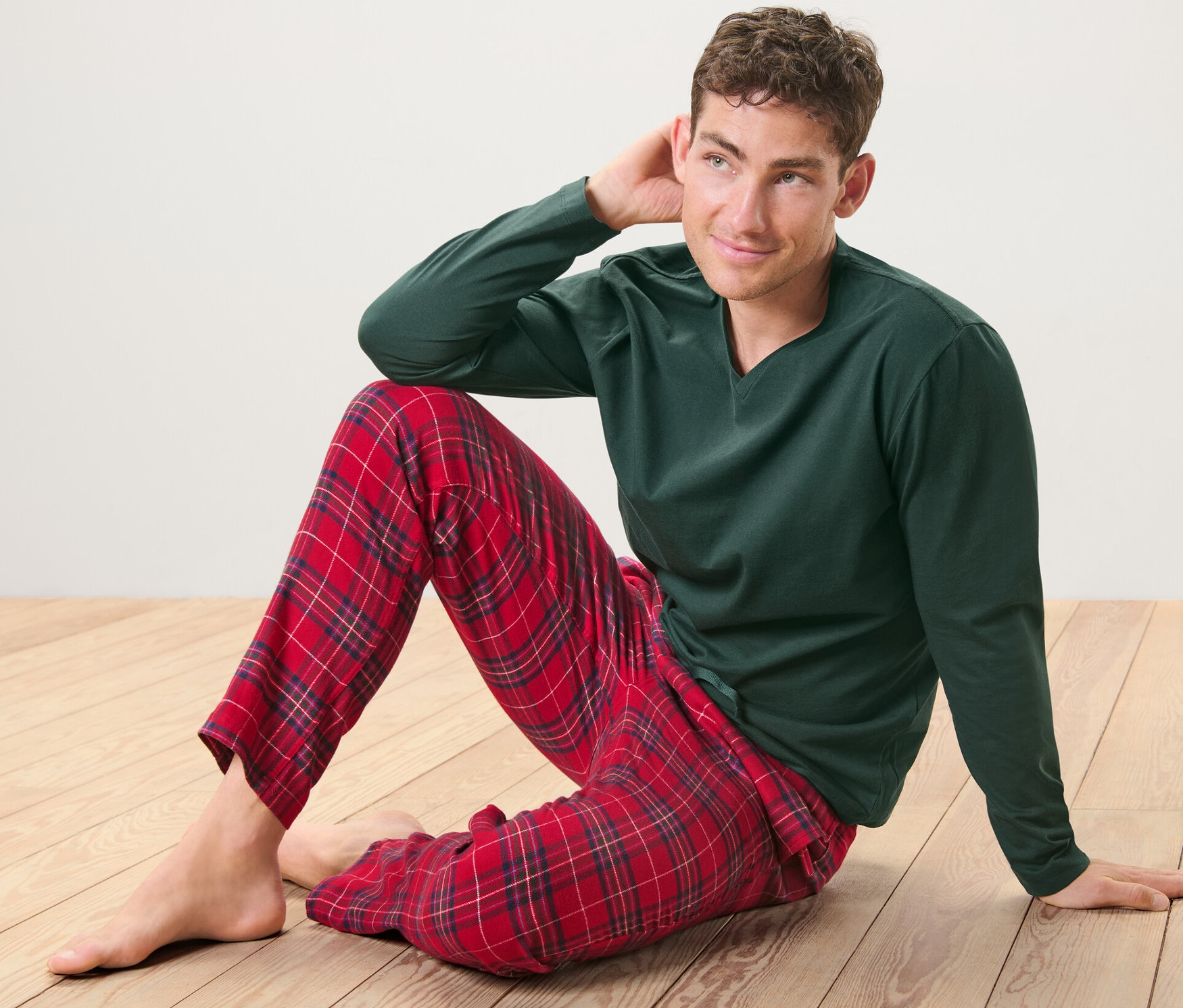 Mężczyzna siedzi na drewnianej podłodze i ma na sobie zieloną piżamę z czerwoną, flanelową spodnią.