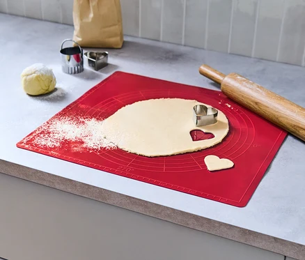 Ciasto jest rozwałkowywane na czerwonej macie do pieczenia, z wyciętym kształtem serca.