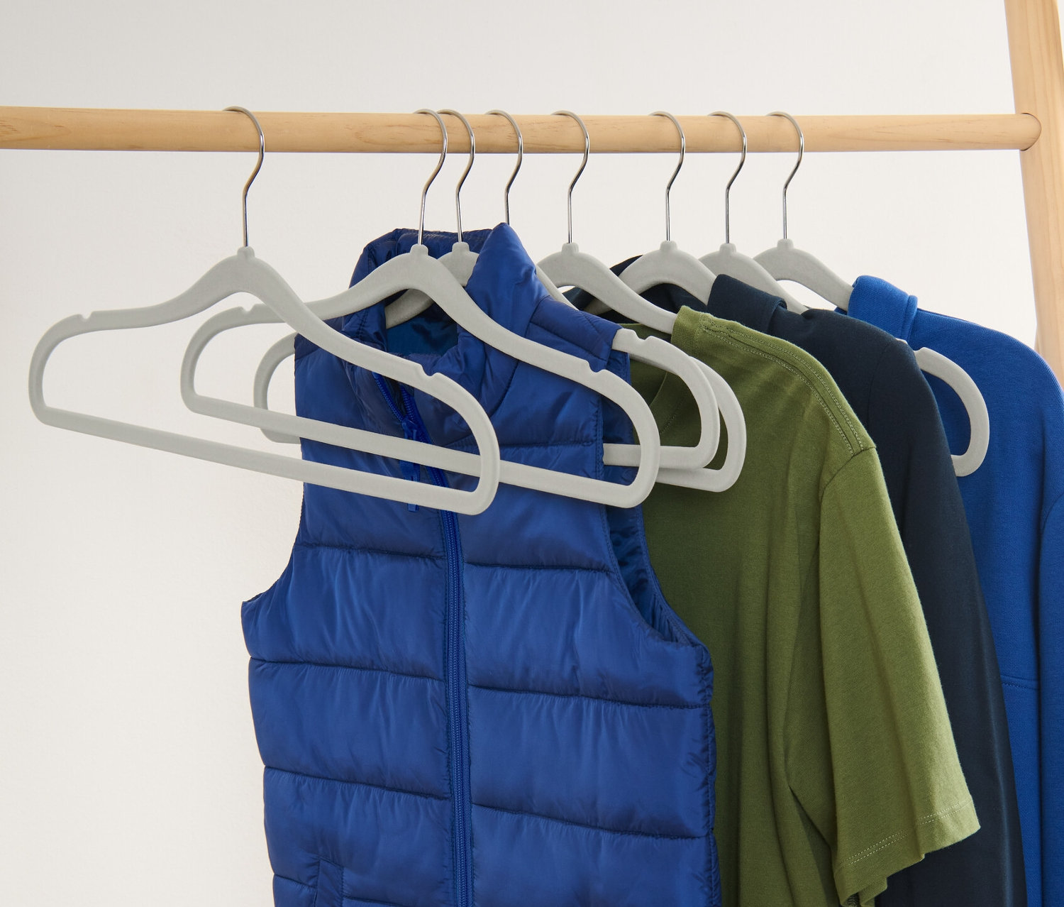 Niebieska kamizelka i kolorowe ubrania wiszą na 8 wyjątkowo wąskich wieszakach.