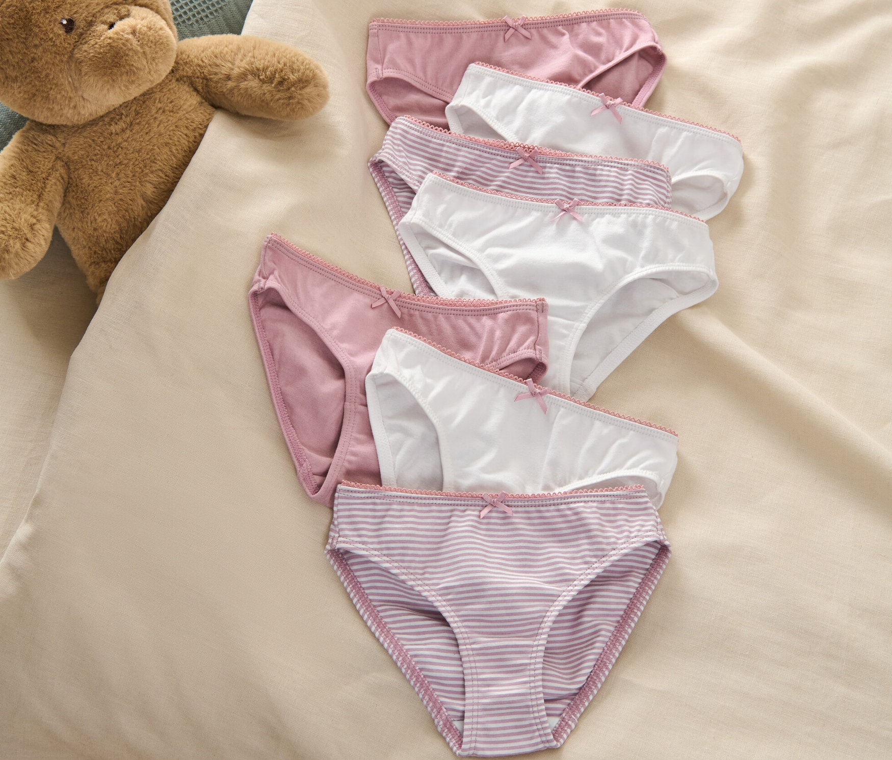 Siedem par fig dziecięcych leży na łóżku obok pluszowego misia.