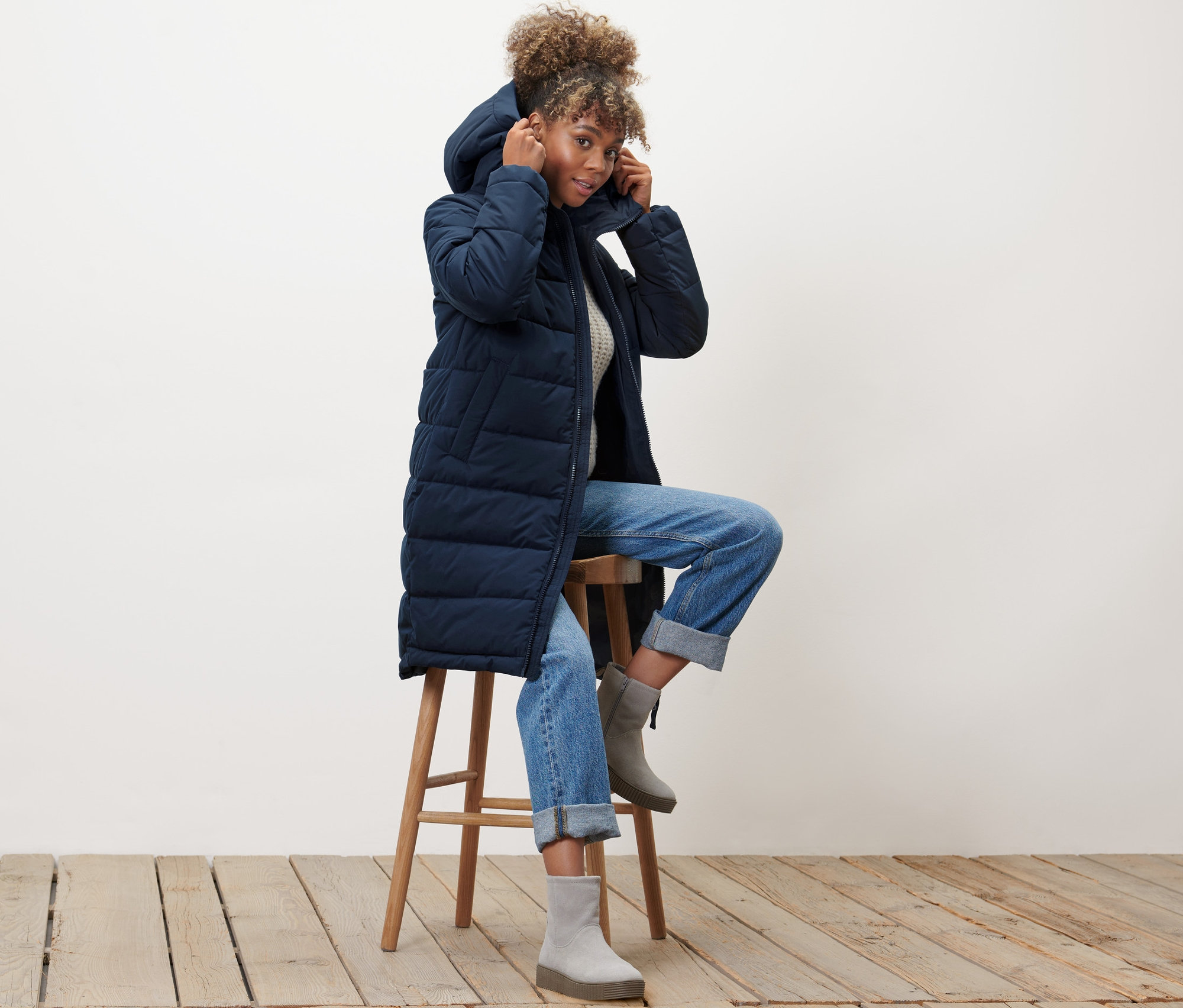 Kobieta siedzi na stołku ubrana w niebieski płaszcz pikowany.