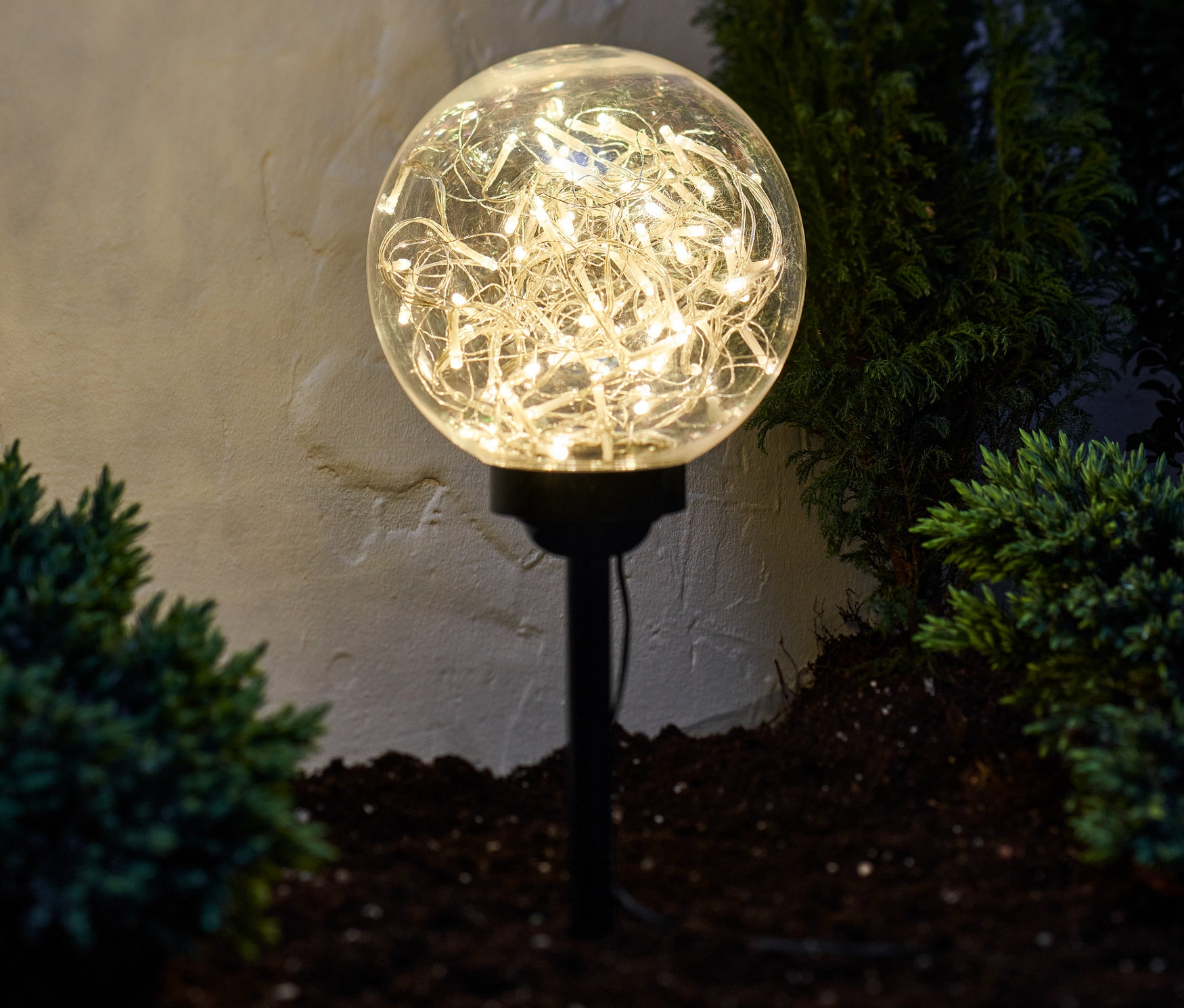 Świecąca kula świetlna LED ze szpikulcem stoi w ogrodzie między krzewami.