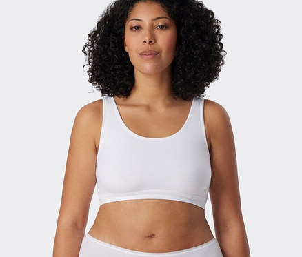 Kobieta ma na sobie białe braletki z bawełną ekologiczną SCHIESSER, 2 sztuki i białe majtki.