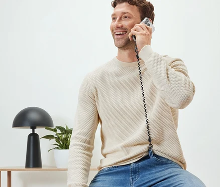 Mężczyzna siedzi i rozmawia przez telefon z łańcuszkiem zabezpieczającym do smartfona.