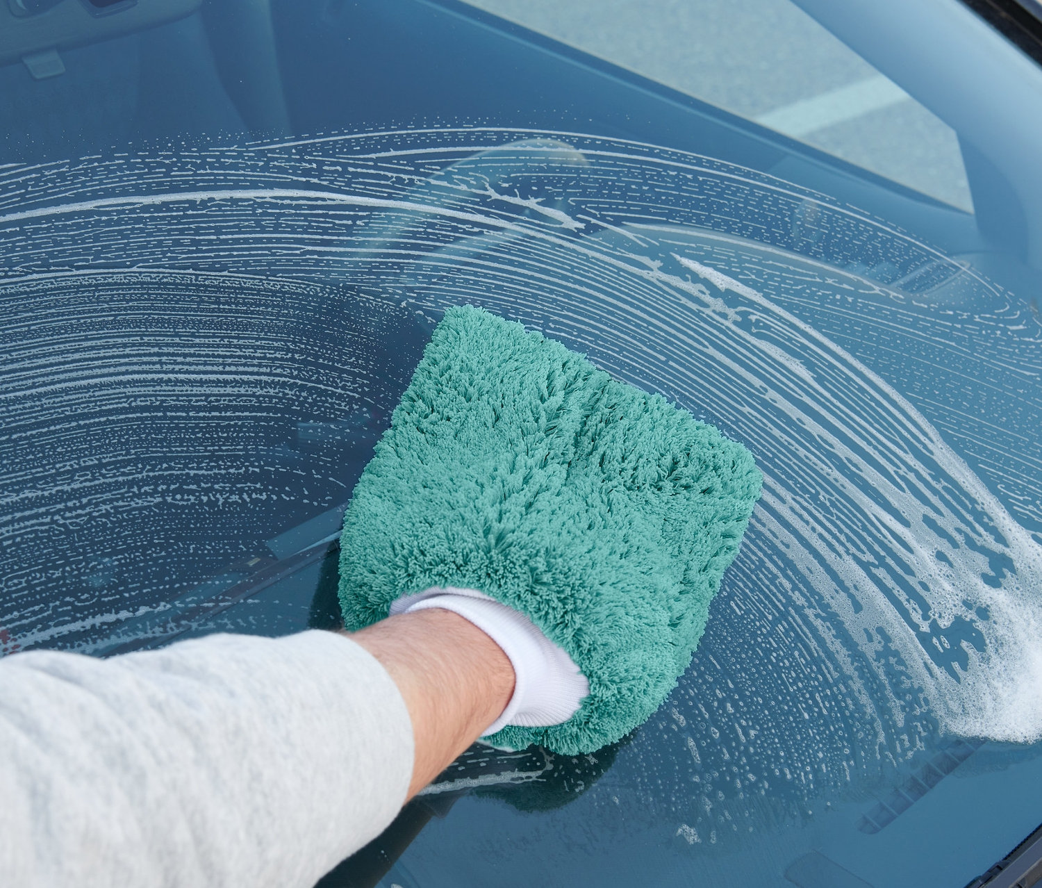 Mężczyzna myje przednią szybę samochodu rękawicą do mycia samochodu.