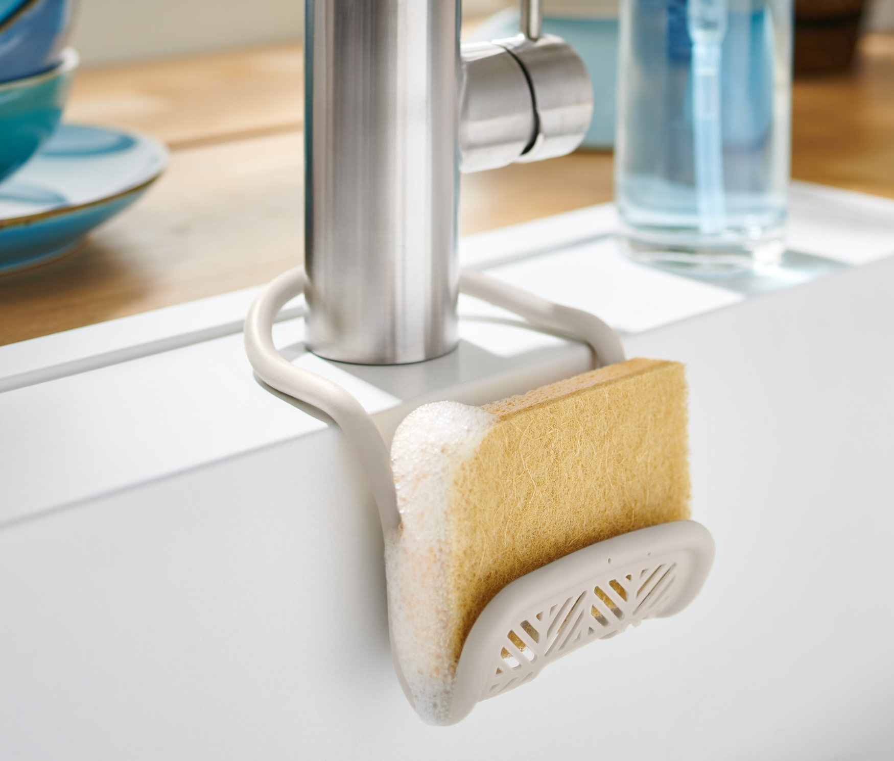 Organizer do zlewu z żółtą gąbką przymocowany do kranu zlewu.