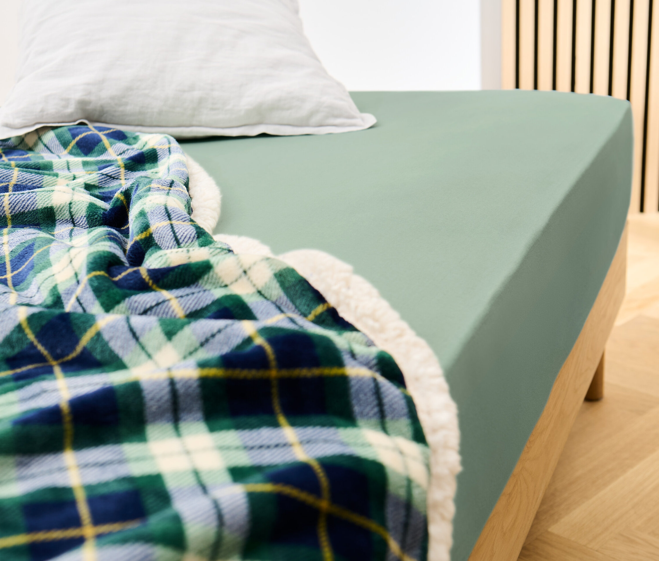 Łóżko z szałwiowym prześcieradłem dżersejowym i kocem w kratę.