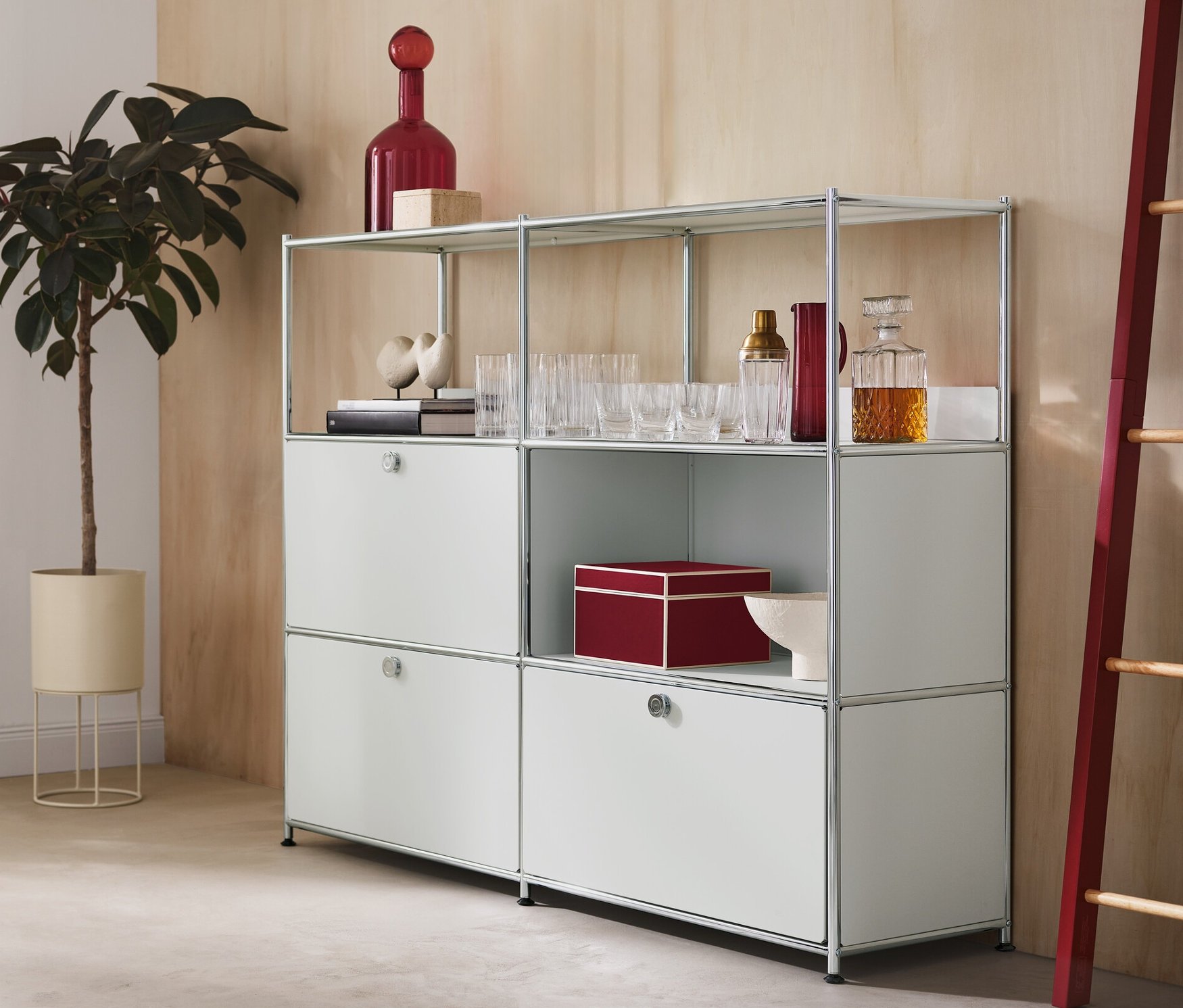 W pokoju znajduje się donica ozdobna z rośliną, metalowa komoda „CN3” z 2 klapami i 1 szufladą oraz dekoracyjna drabina z czerwonymi elementami bocznymi.