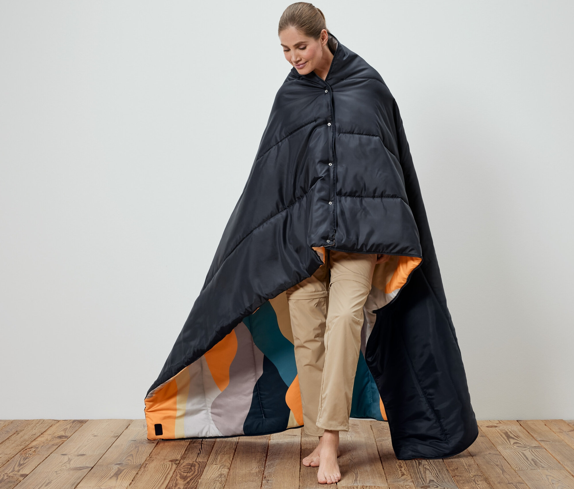 Kobieta owinięta czarnym śpiworem-kołdrą 4 w 1. Wnętrze śpiwora jest wzorzyste.