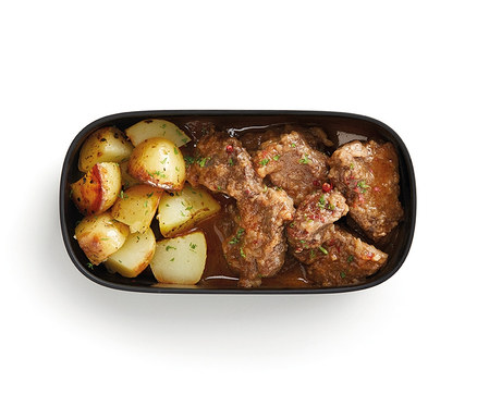 Widok z góry na zestaw pojemników na lunch ze sztućcami, zawierający pieczone ziemniaki i mięso w sosie.