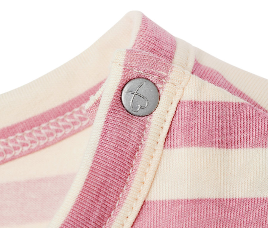 Zbliżenie na niemowlęcą sukienkę dżersejową w różowo-kremowe paski z srebrnym guzikiem w kształcie serca.