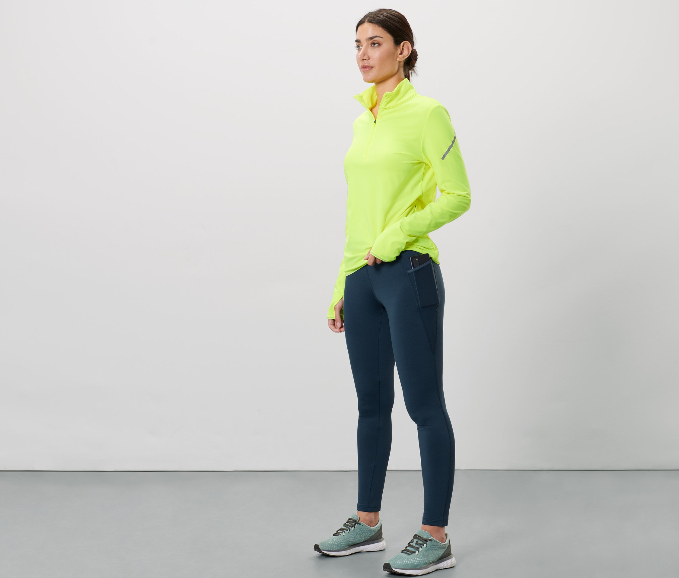 Kobieta ma na sobie granatowe ciepłochronne legginsy do biegania i neonowożółtą bluzkę.