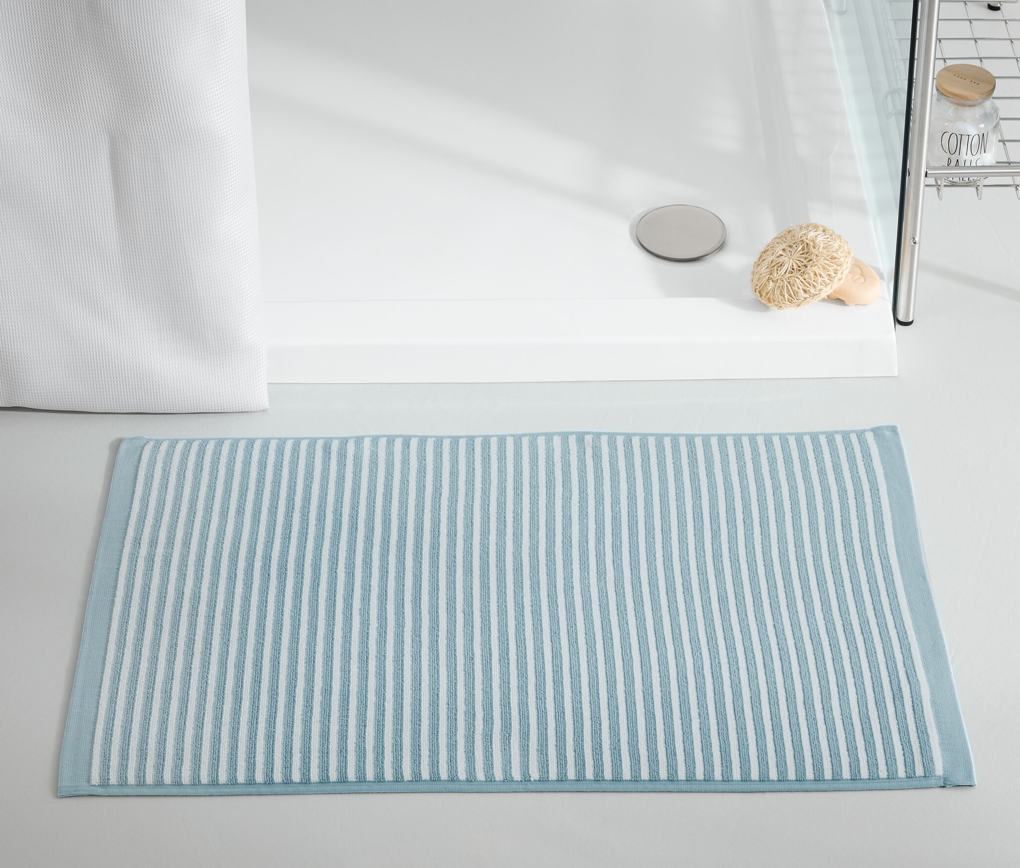 Niebieski dywanik łazienkowy leży przed kabiną prysznicową.