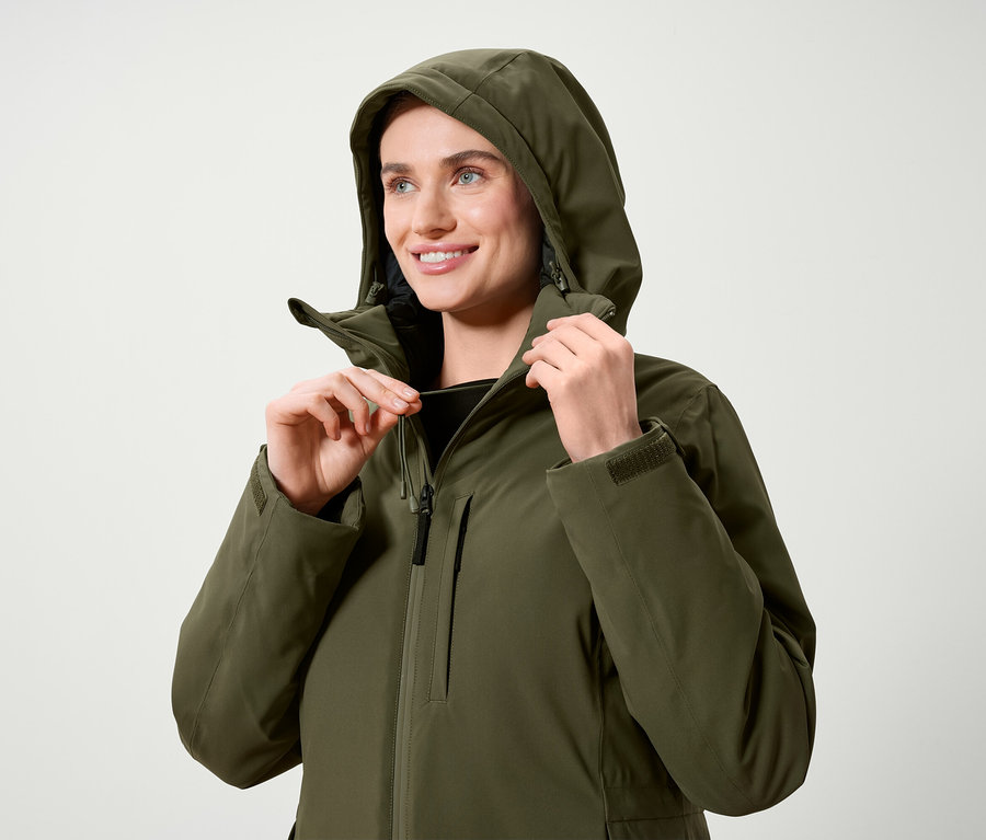Kobieta reguluje kaptur oliwkowozielonej kurtki.