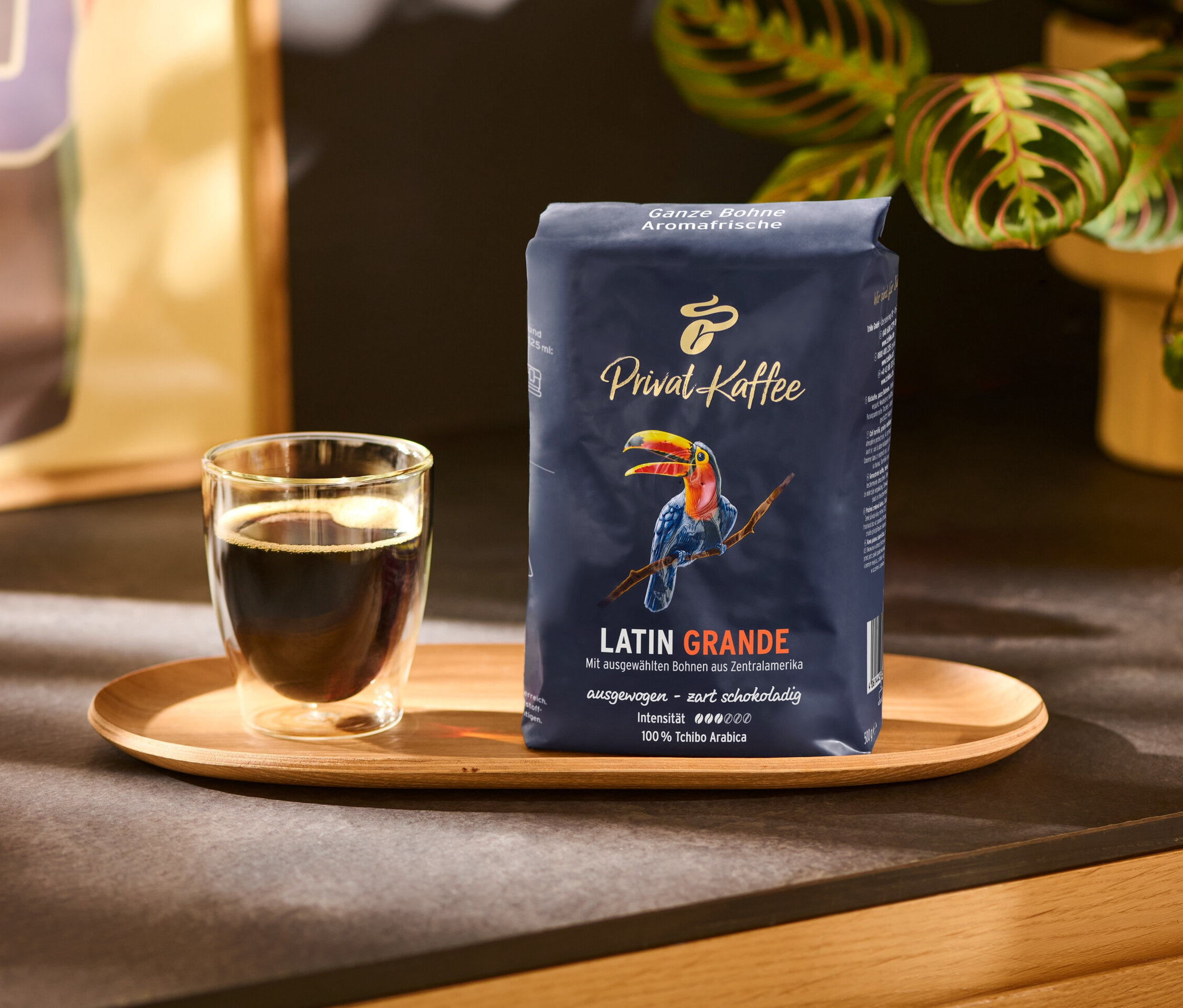 Filiżanka kawy i opakowanie Privat Kaffee, Latin Grande, 500 g, kawa w ziarnach na drewnianej tacy.