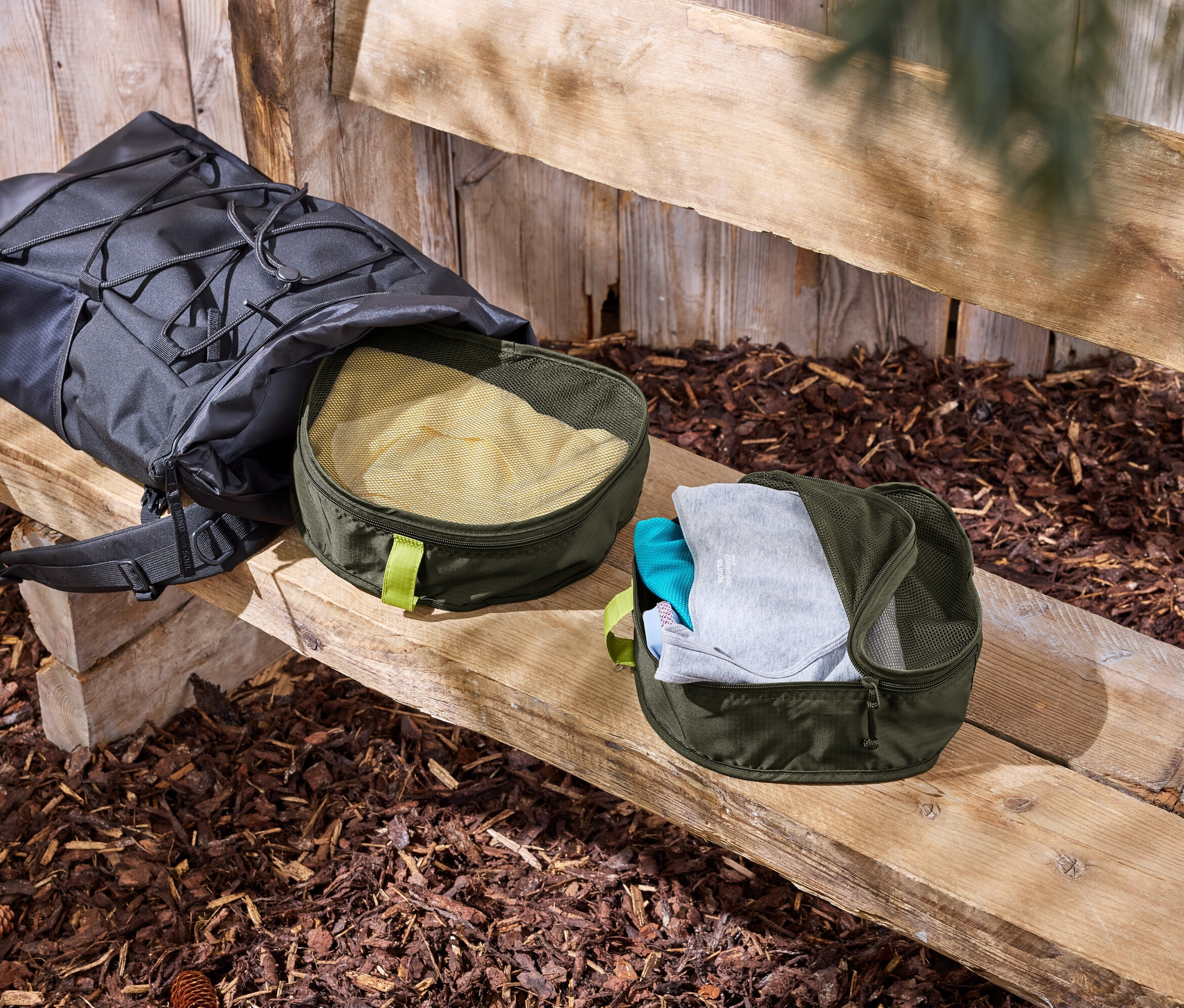 Czarny plecak leży na drewnianej ławce obok dwóch zielonych organizerów na ubrania.