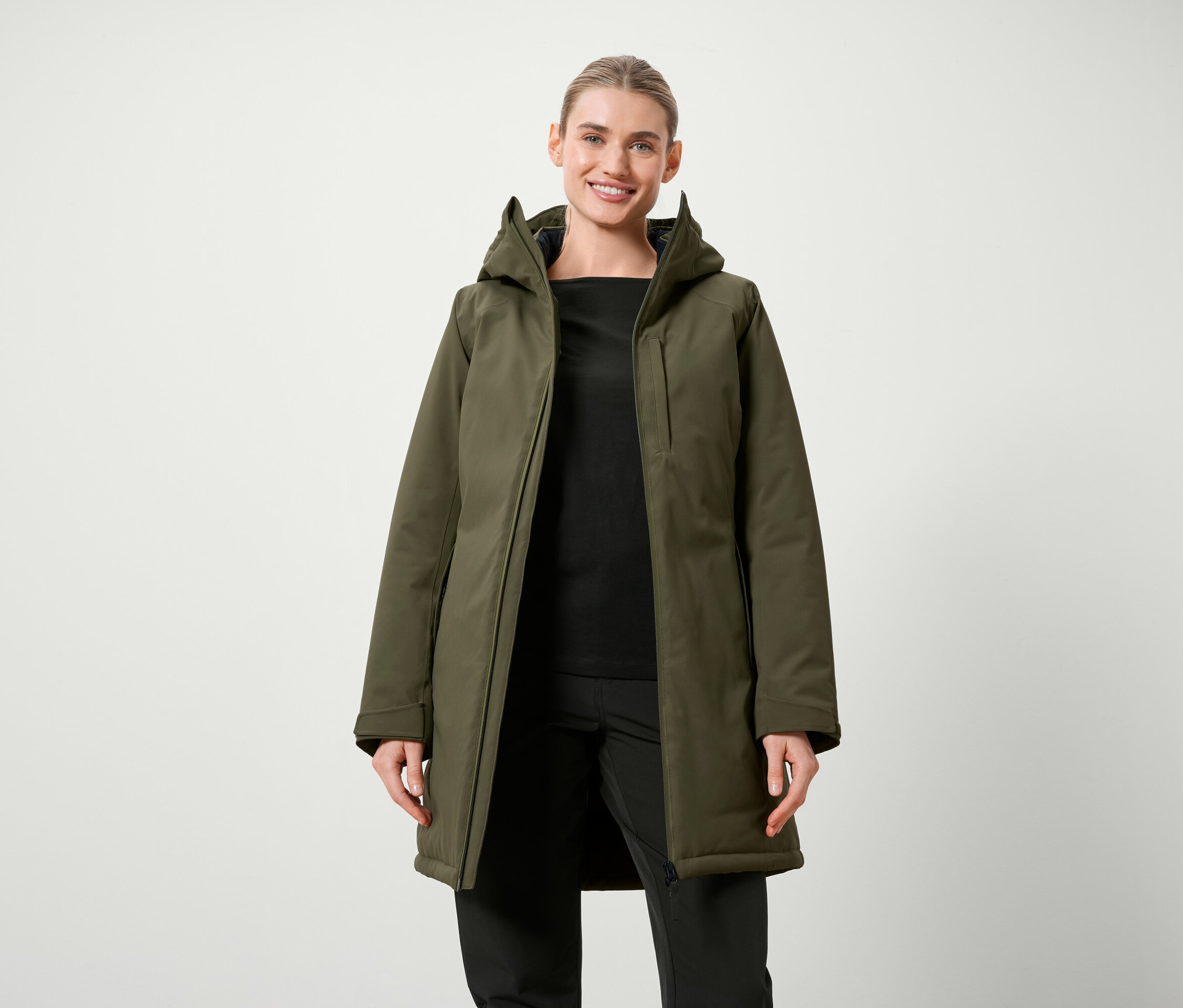 Kobieta pozuje w oliwkowozielonej kurtce z kapturem i czarnych ubraniach.