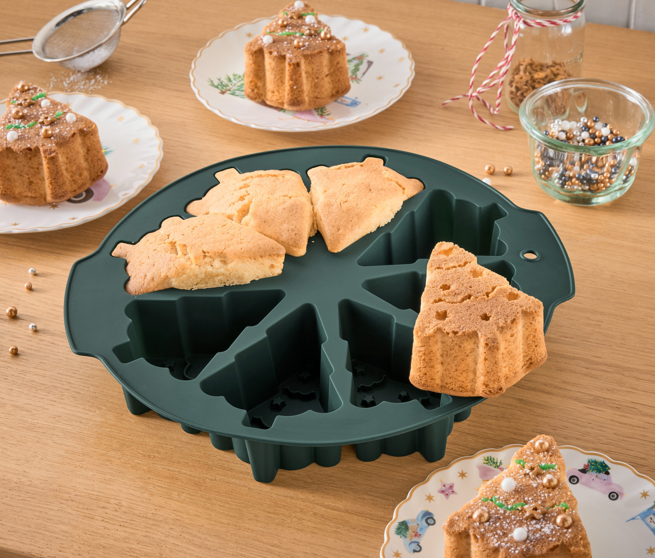 Forma do pieczenia w kształcie choinki z upieczonymi ciastami i udekorowanymi ciastami na talerzach.