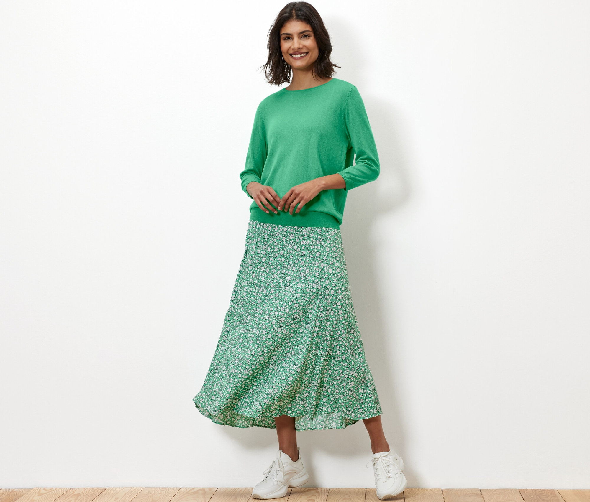 Kobieta ma na sobie zielony, cienki sweter z jedwabiem i kwiecistą spódnicę.