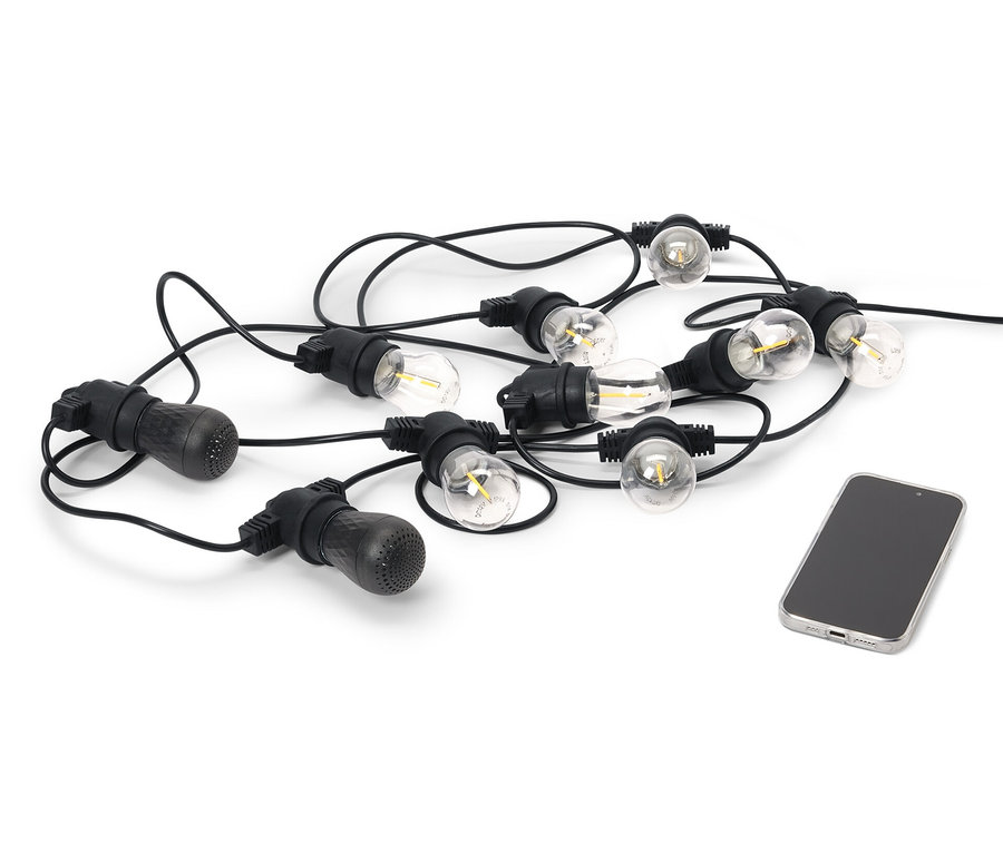 Czarny łańcuch świetlny LED z dwoma głośnikami Bluetooth® do użytku na zewnątrz leży obok telefonu komórkowego na białym tle.