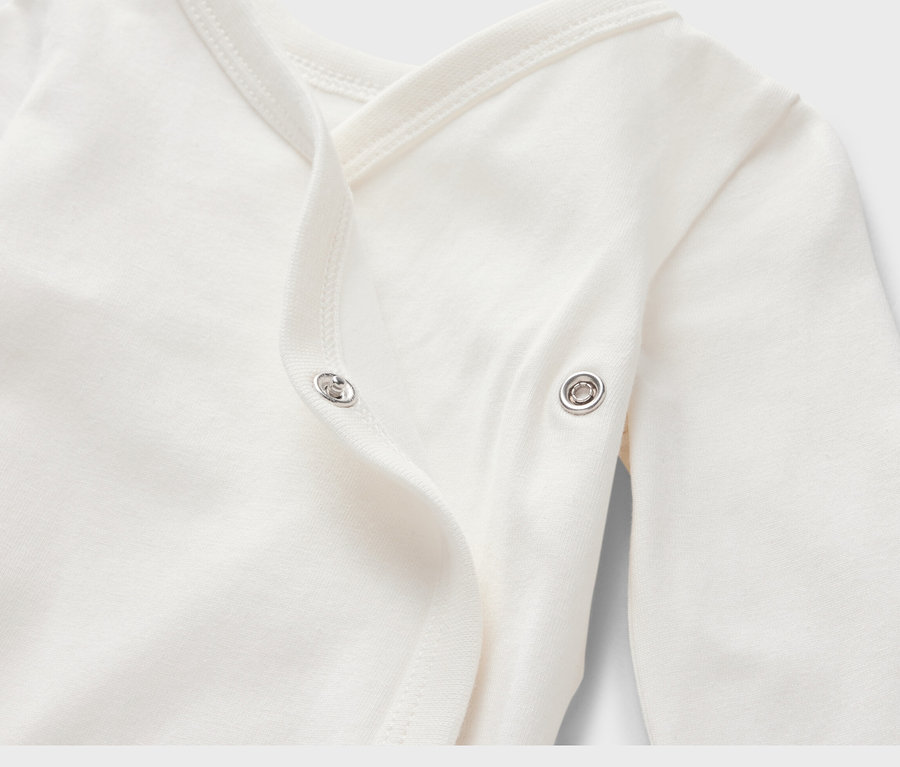 Zbliżenie na białe body niemowlęce z długim rękawem, zapinane na zatrzaski.