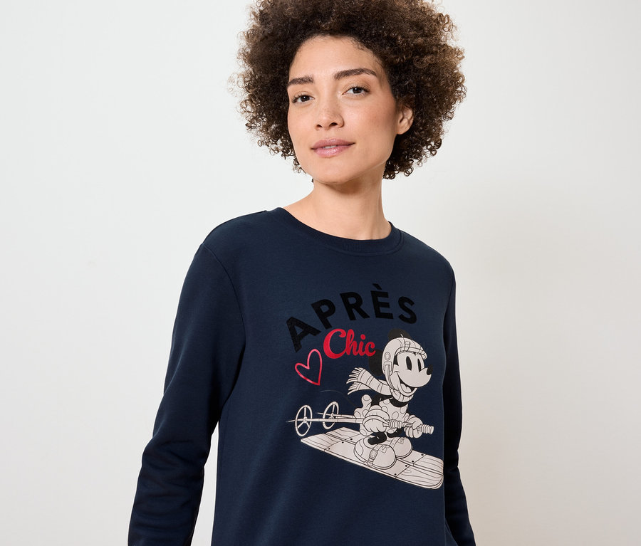 Kobieta ma na sobie granatowy sweter z nadrukiem Myszki Miki na snowboardzie.