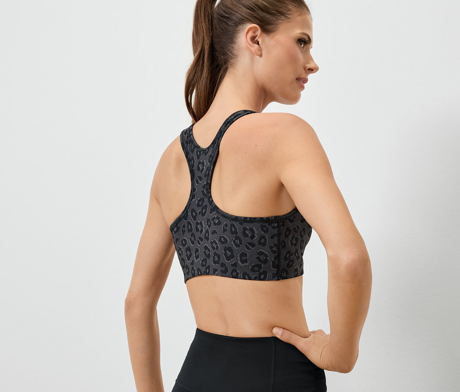Kobieta tyłem do kamery ma na sobie stanik sportowy we wzór zwierzęcy i czarne legginsy.
