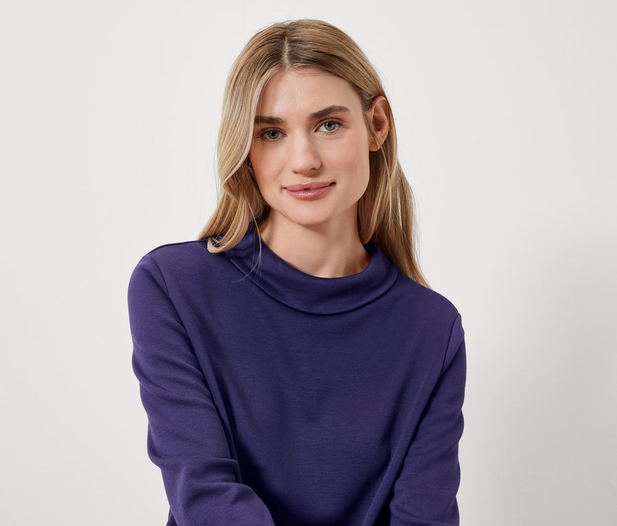 Portret kobiety o blond włosach w niebieskim golfie.