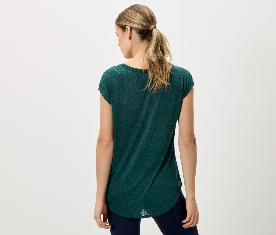 Widok z tyłu kobiety z blond włosami, ubranej w zielony T-shirt i niebieskie spodnie.